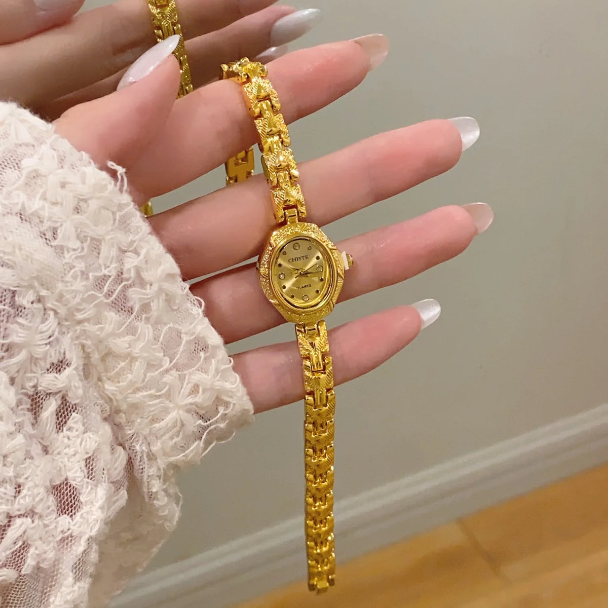 A hand is holding a gold-toned quartz fashion wristwatch with a yellow gold chain and bracelet.