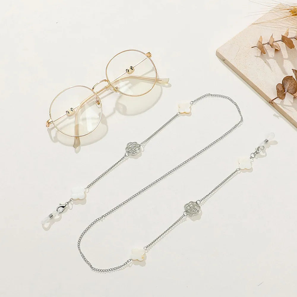 A delicate silver chain necklace featuring pearl and clear gemstone charms, displayed next to a pair of round metal-framed ey