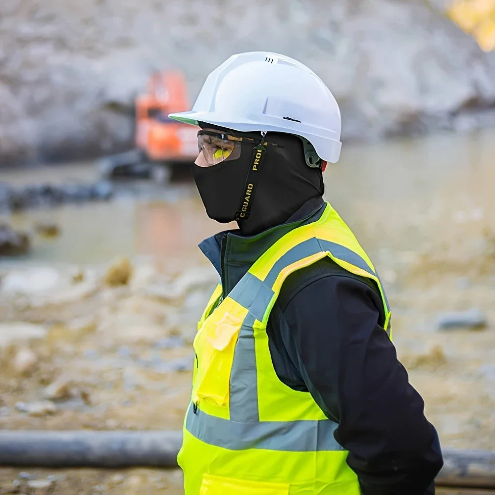 A person wearing a white hard hat, clear goggles, and a black balaclava and high-visibility vest is visible outdoors.