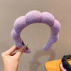 A hand is holding a purple cloud sponge hair accessory headband against a light background.
