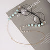 Gold-toned pearl beaded eyewear chains displayed on a gray card with text.