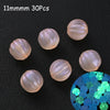 Thirty 11mm luminous glow-in-the-dark acrylic beads scattered on a dark surface with a cluster of blue and green beads.