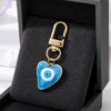 A gold-colored keychain featuring a heart charm with a blue and white Turkish evil eye design, displayed in a black velvet bo